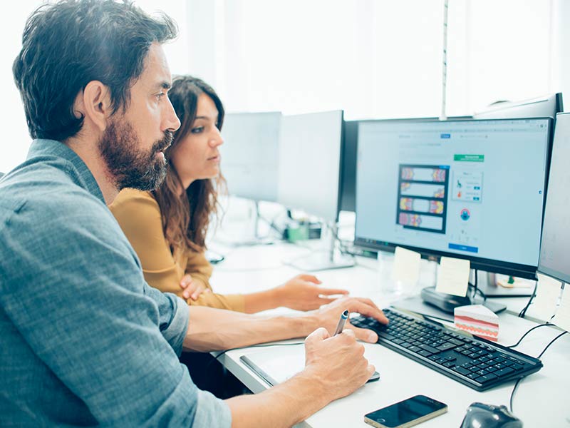 Office picture with man and woman sitting at computer
